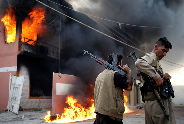 Kurdish gunmen hold their rifles in front of a burning house of a Shi'ite militiaman during clashes in Tuz Khurmato.&nbsp;(Goran Tomasevic/Reuters)</p>  