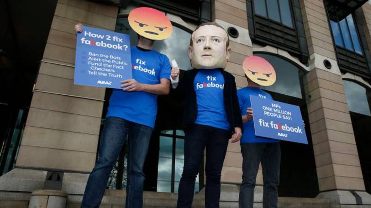 A protester wearing a mask with the face of Facebook founder Mark Zuckerberg, in between men wearing angry face emoji masks, protest Facebook outside Portcullis in 2018. (Alastair Grant/AP file)