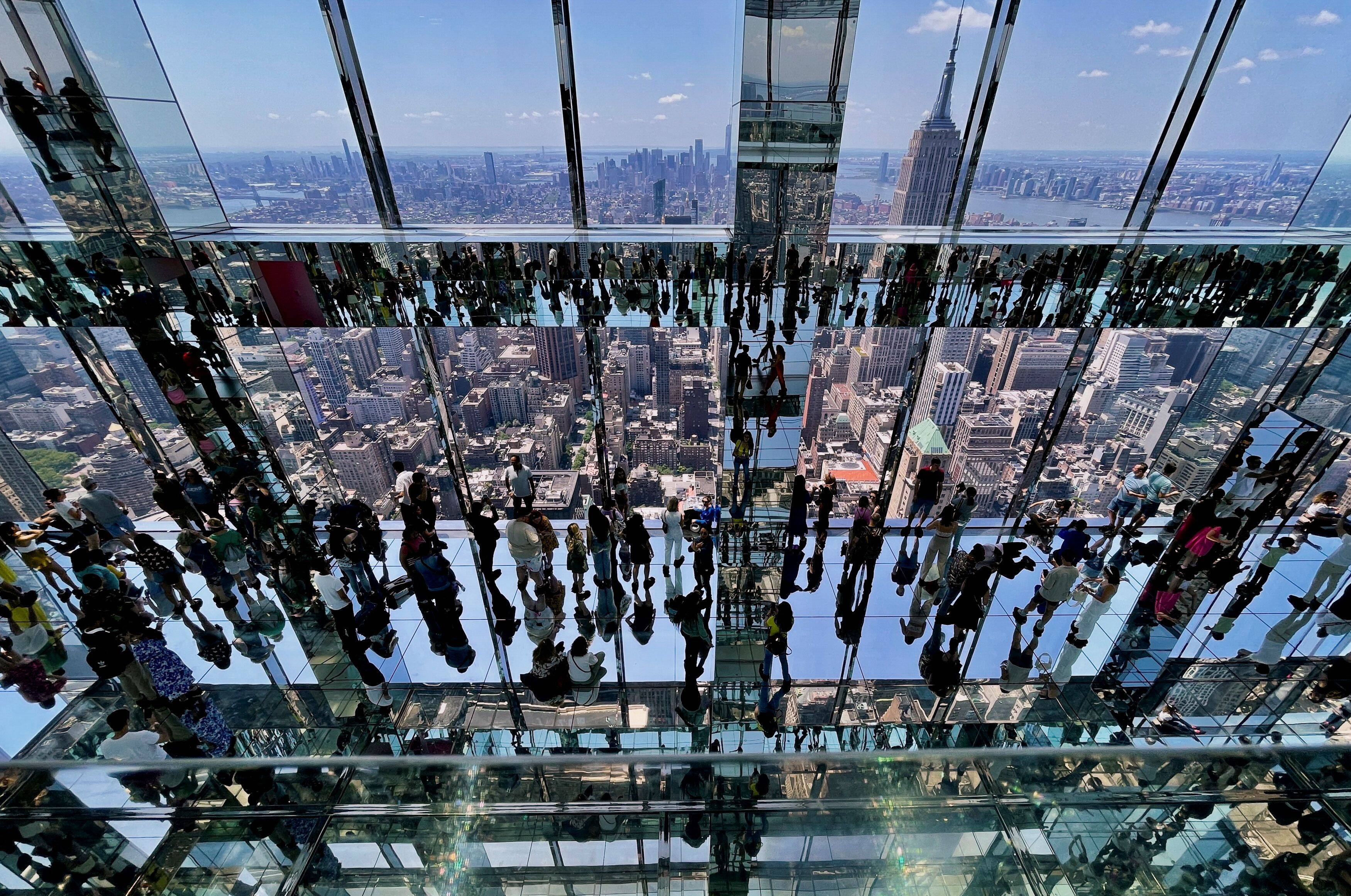 Visitors are reflected in the many mirrored surfaces, floors and ceilings as they look out at Manhattan and the Empire State Building from the SUMMIT observation deck atop the new One Vanderbilt tower in midtown Manhattan on May 30. (Reuters/Jim Bourg)