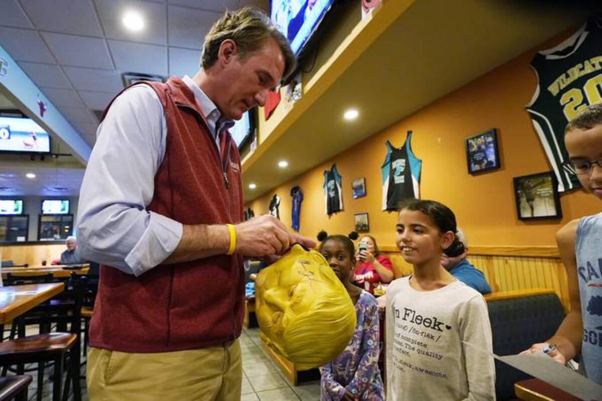 Glenn Youngkin signs a Donald Trump Halloween mask for a fan during a meet and greet at a sports bar in Chesapeake, Va. (AP Photo/Steve Helber)