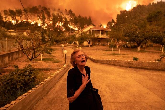 An elderly resident reacts as a wildfire approaches her house in the village of Gouves, on the Greek island of Evia, on Aug. 8. (Konstantinos Tsakalidis/Bloomberg)