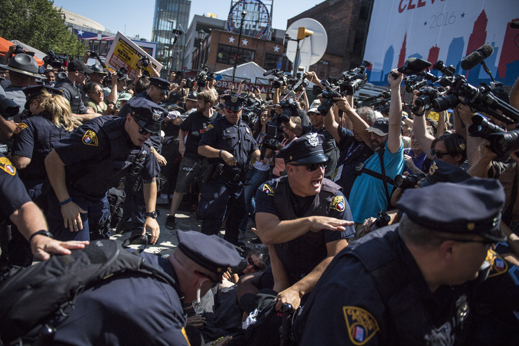 Officers arrest protestors after a demonstrator set an American flag on fire at the main entrance of the Quicken Loans Arena. (Jabin Botsford/The Washington Post)</p>  