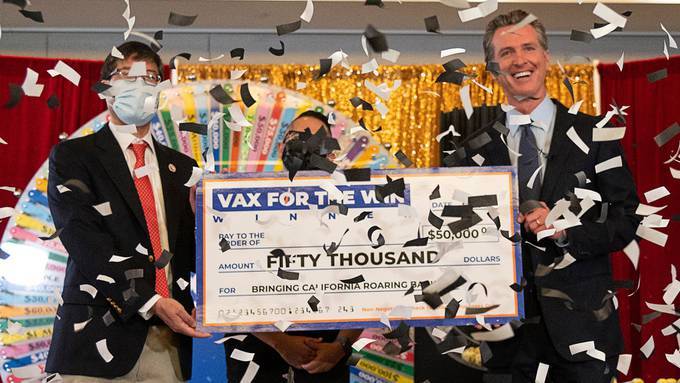 California Gov. Gavin Newsom, right, and State Sen. Richard Pan, left, hold a mock check with UC Davis assistant nurse manager Claudio Alvarado last month as part of a coronavirus vaccine promotion. (Paul Kitagaki Jr./Sacramento Bee)