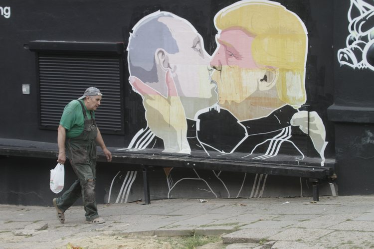 A man passes by a graffiti mural in&nbsp;Lithuania&nbsp;that depicts&nbsp;Donald Trump kissing Vladimir Putin outside a barbecue&nbsp;restaurant earlier this month. (Valda Kalnina/EPA)</p>  