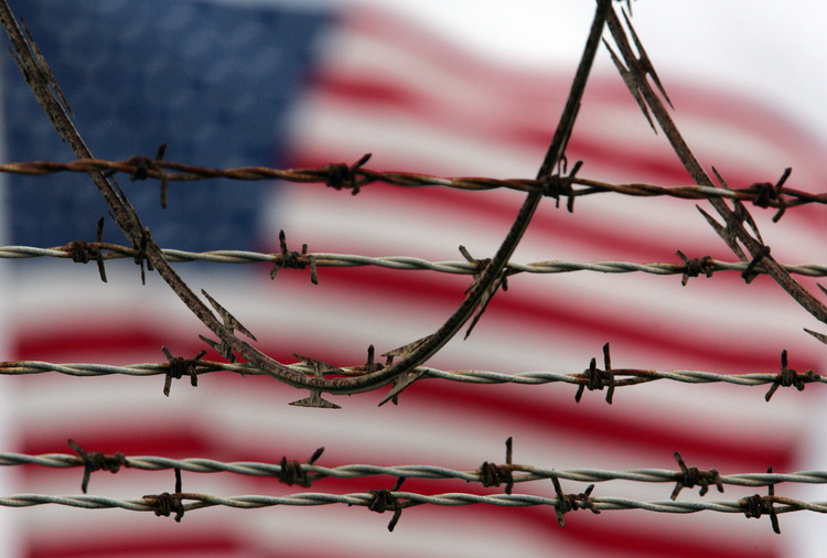 An American flag flies behind the barbed and razor wire at the Camp Delta detention facility at Guantanamo Bay, Cuba. (Brennan Linsley/AP)</p>  