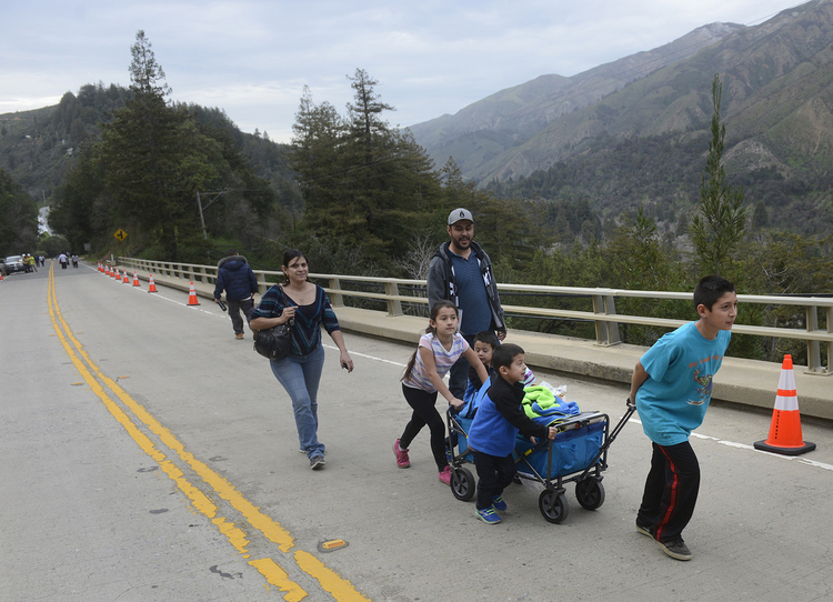 A family pulls a wagon of groceries across the storm-damaged Highway 1 that has made Big Sur "an island." (David Royal/AP)</p>  