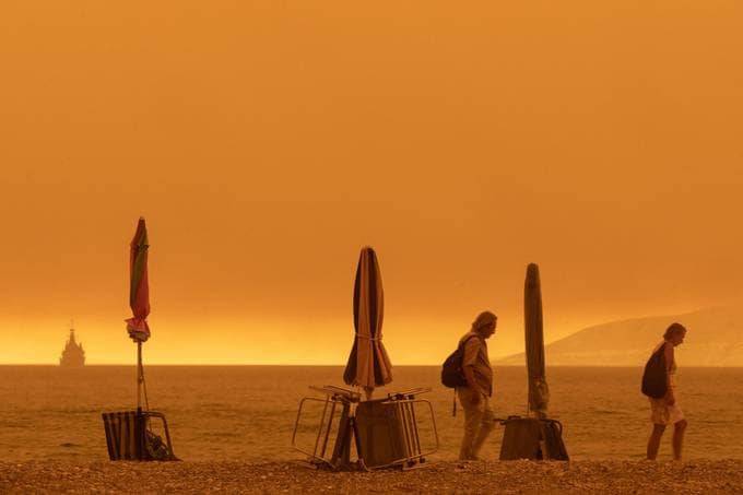 People walk on the beach as thick smoke covers the Greek island of Evia on Aug. 8. (Konstantinos Tsakalidis/Bloomberg)