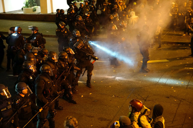 A police officer sprays the crowd with an irritant during a protest against Trump in Portland on Saturday. (William Gagan/Reuters)</p>  