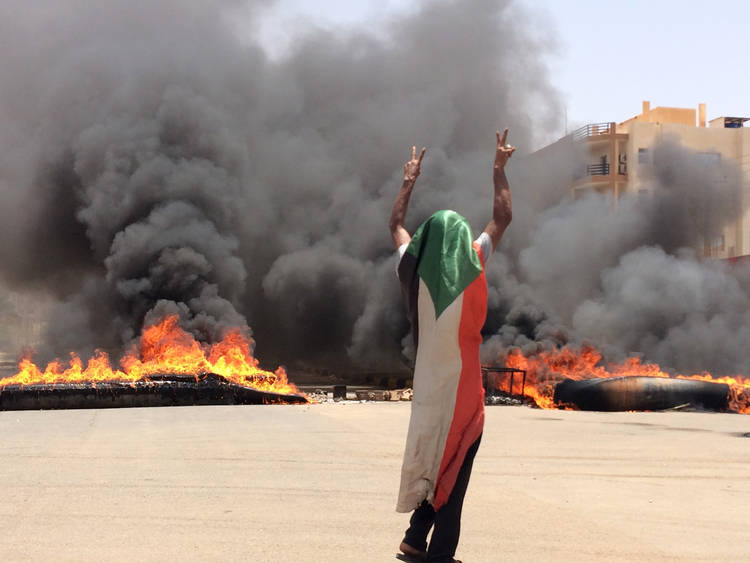 A protester wears a Sudanese flag in front of burning tires and debris after a protest was dispersed violently outside the army headquarters in Khartoum on June 3. (AP)  