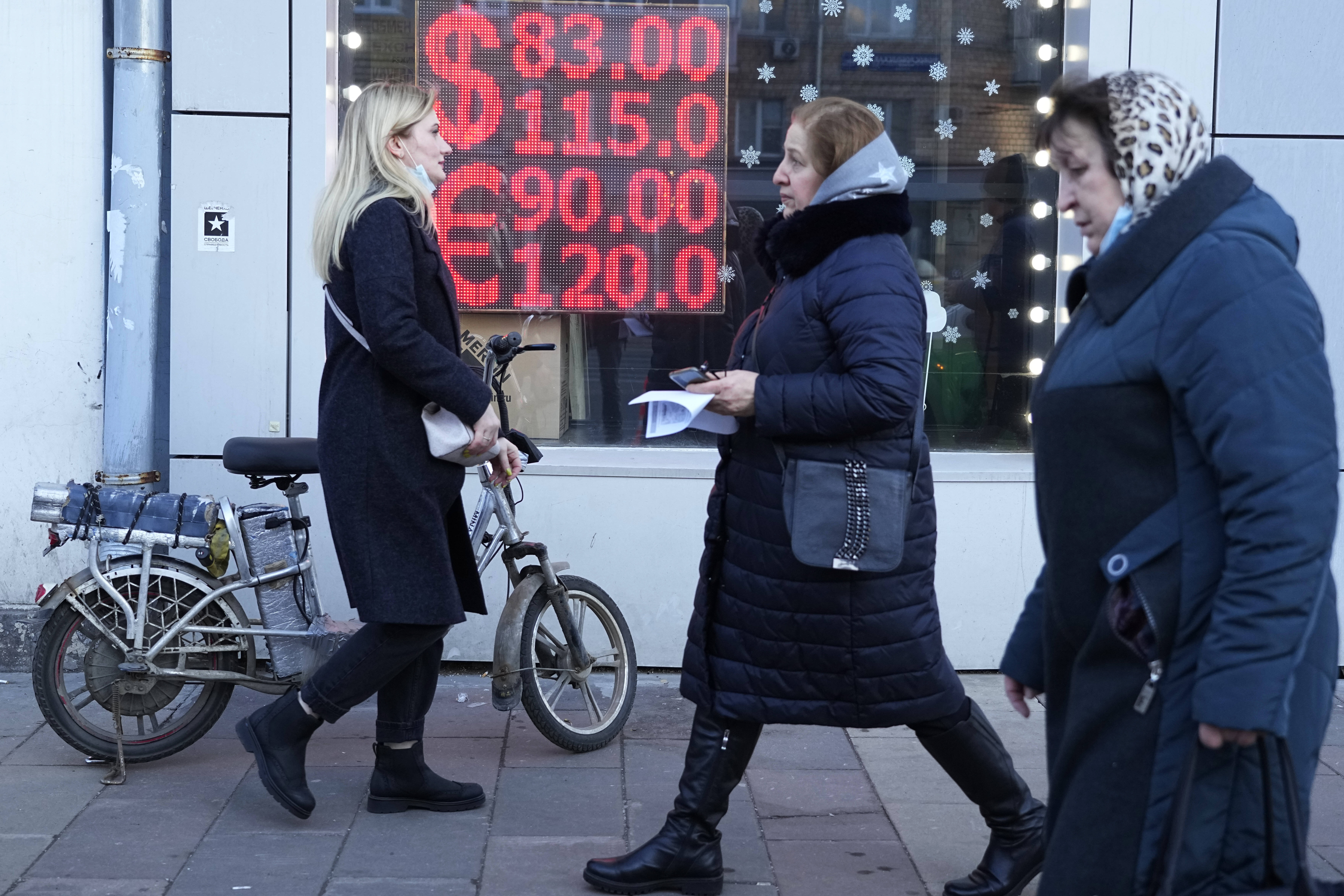 People walk past a currency exchange office screen displaying the exchange rates of the U.S. dollar and euro to Russian rubles in Moscow on Feb. 28. (Pavel Golovkin/AP)