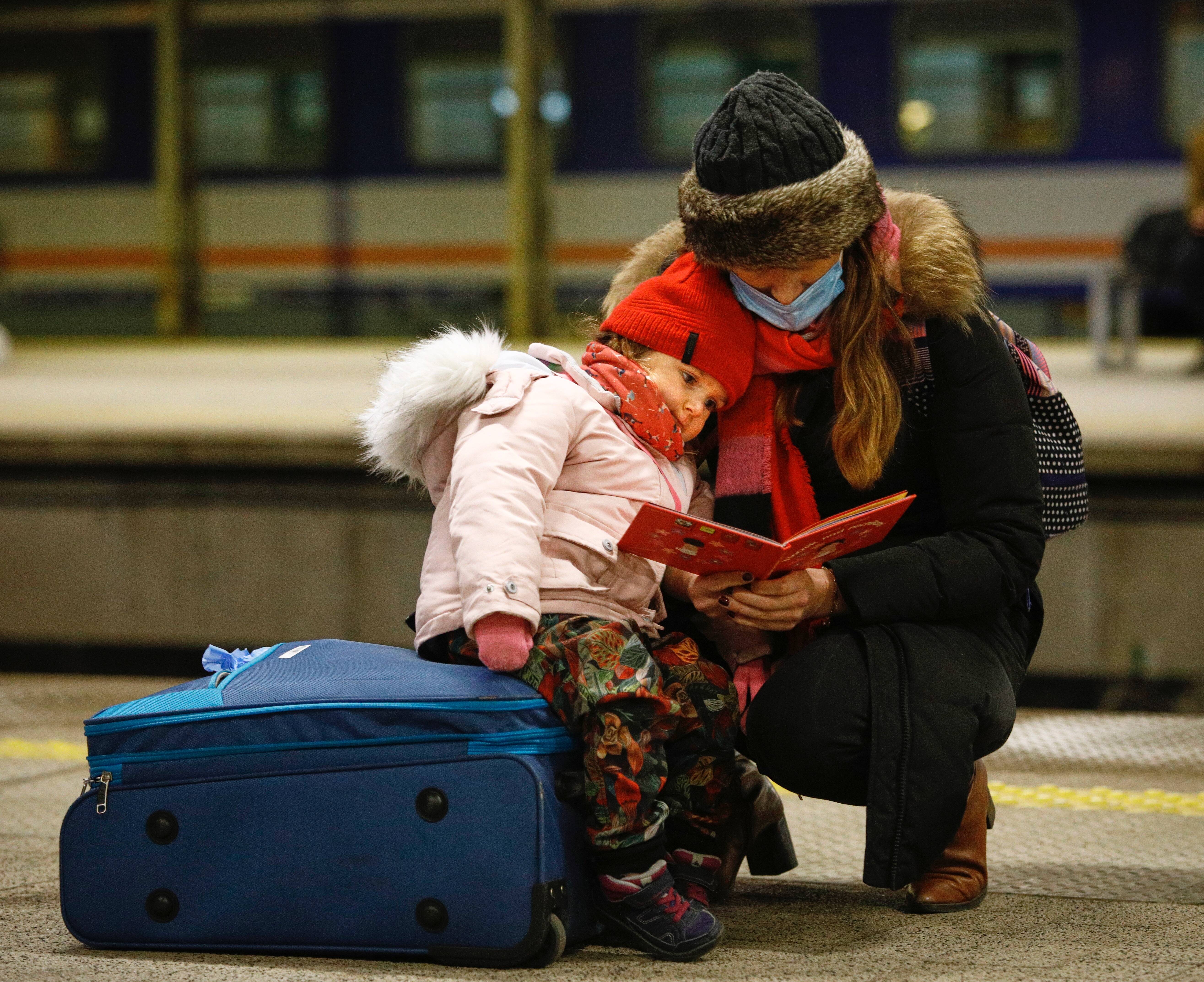 A woman reads a book while holding a child after the arrival of a train with 350 refugees from Kyiv, Ukraine at the Warsaw East train station in Poland on March, 4, 2022. (Photo by STR/NurPhoto via Getty Images)