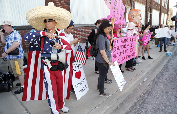 A man draped in the U.S. flag&nbsp;protests outside Trump's&nbsp;rally in Dallas.&nbsp;(Stewart F. House/Getty Images)</p>  