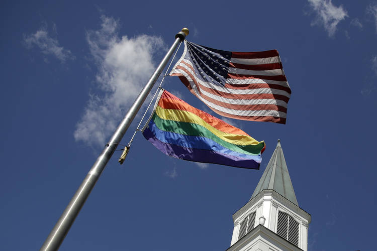 A gay pride flag flies along with the U.S. flag in front of the Asbury United Methodist Church in Prairie Village, Kan. (Charlie Riedel/AP)  