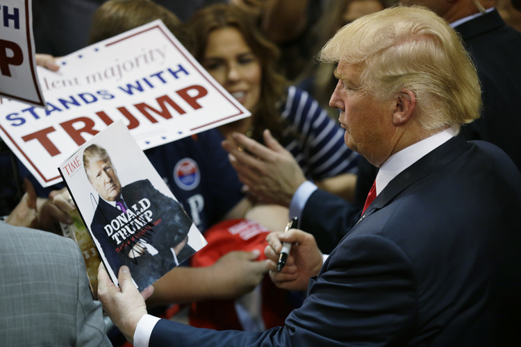 Trump looks at his photo on a magazine cover as he signs autographs in Eugene, Ore. (AP/Ted S. Warren)</p>  