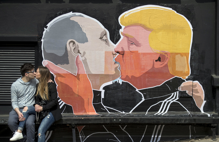A couple kisses in front of graffiti depicting Putin and Trump on the walls of a bar in Vilnius, Lithuania, last May. (Mindaugas Kulbis/AP)</p>