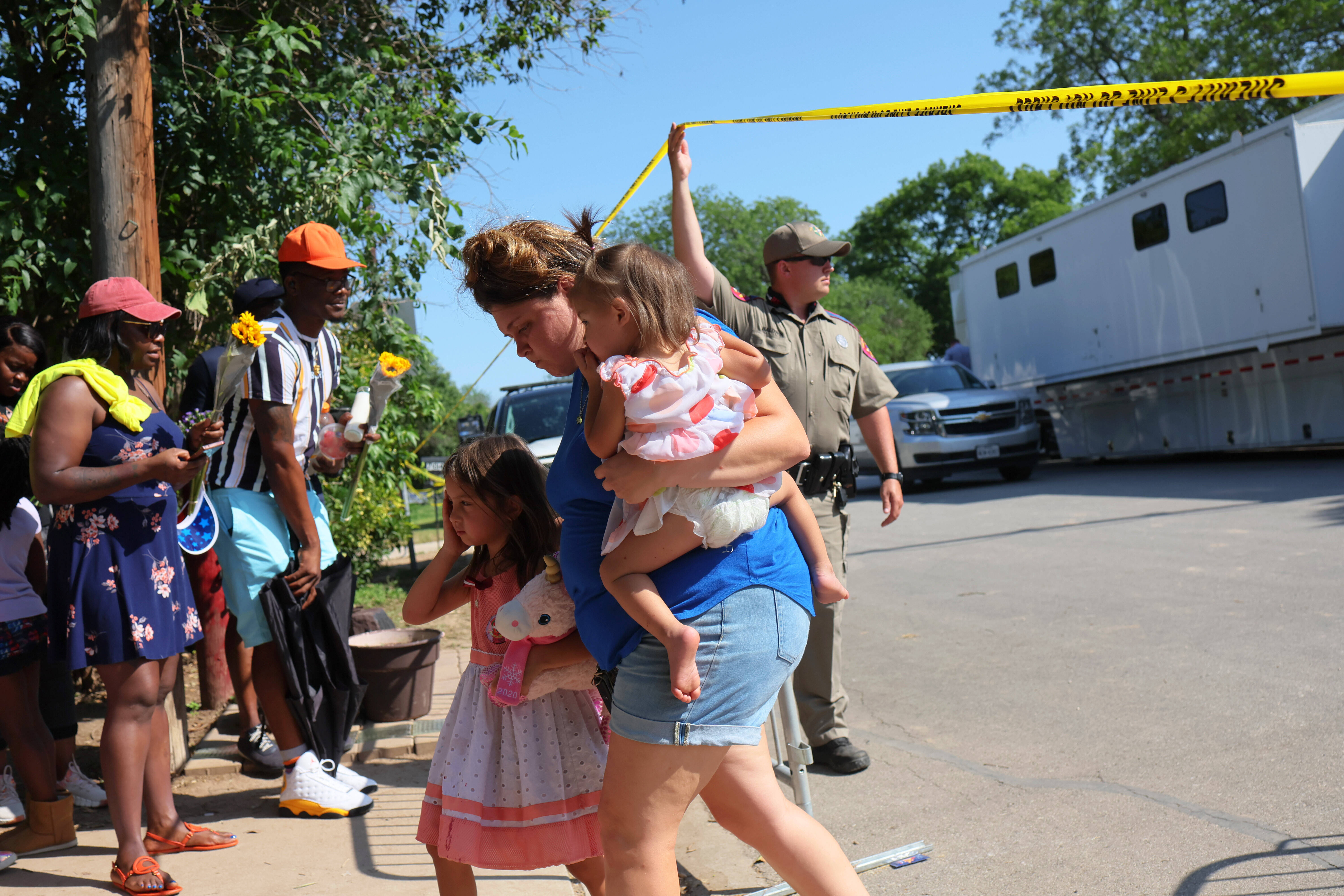 A trooper lifts crime-scene tape to allow people to visit a memorial at Robb Elementary in Uvalde, Tex., on Saturday. (Michael M. Santiago/Getty Images)