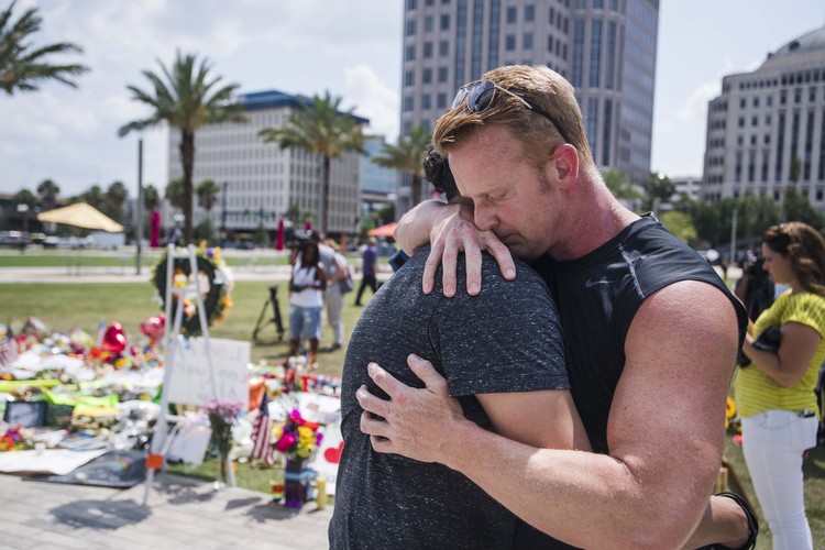 Christian Natal, left, and Cristian Michaels embrace in front of a memorial for the Orlando shooting victims on the front lawn of the Dr. Phillips Center for the Performing Arts. (Amanda Voisard/For the Washington Post)</p>  