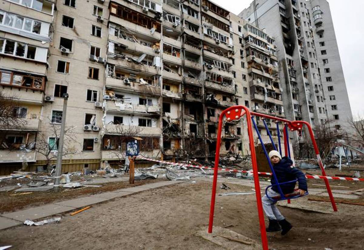 A child sits on a swing in front of a damaged residential building, after Russia launched a massive military operation against Ukraine, in Kyiv. (REUTERS/Umit Bektas)