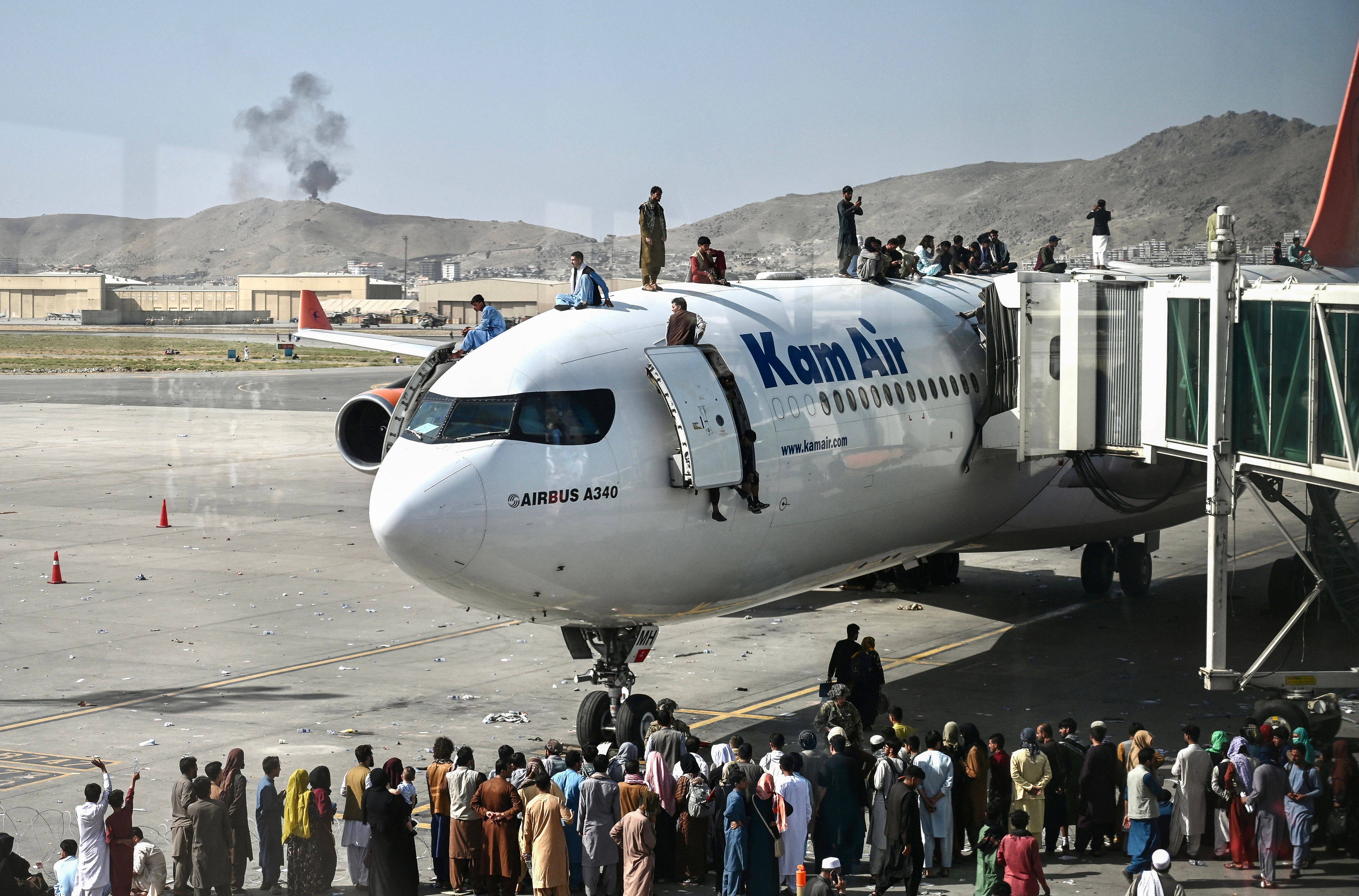 Afghan people climb atop a plane as they wait at the Kabul airport on Monday to get out of the country. (WAKIL KOHSAR/AFP via Getty Images)