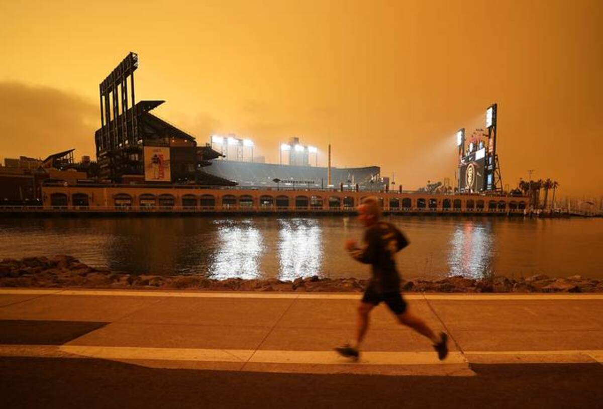 A jogger runs along McCovey Cove outside Oracle Park in San Francisco, under darkened skies from wildfire smoke. (Tony Avelar/AP)
