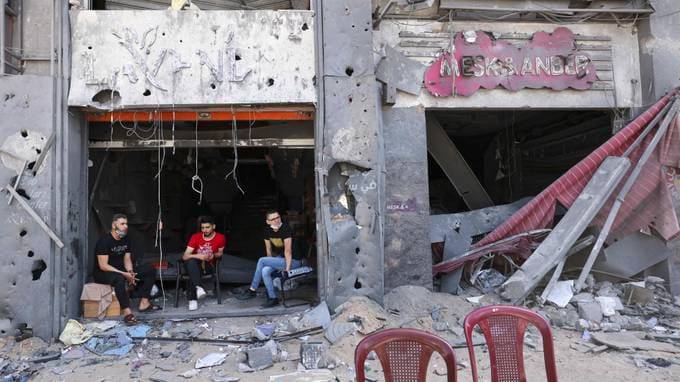 Palestinian shop owners sit at the entrance of their damaged store in Gaza City on Saturday. (Emmanuel Dunand/AFP via Getty Images)