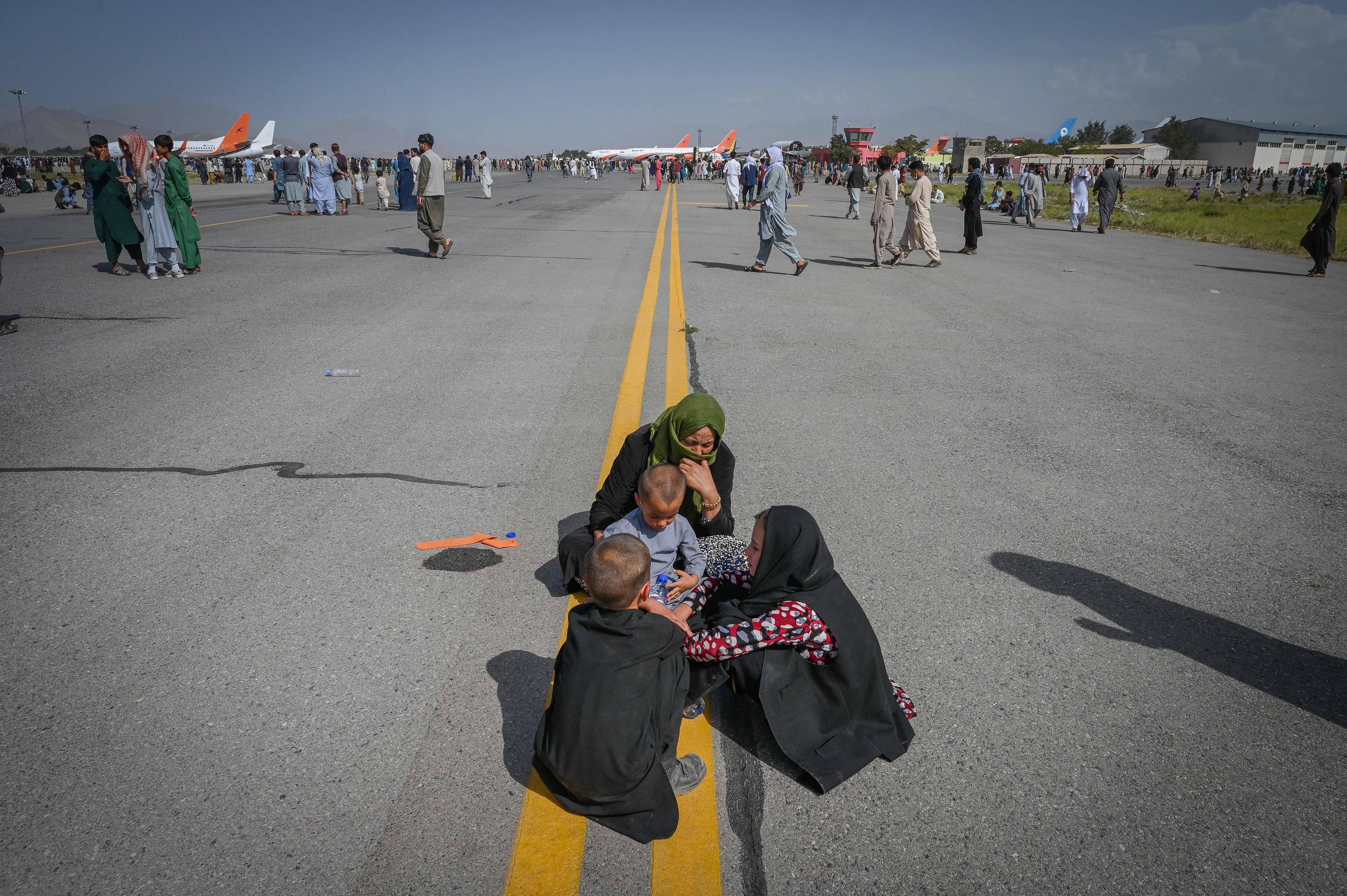 Afghan people sit along the tarmac as they wait to leave Kabul on Monday. (WAKIL KOHSAR/AFP via Getty Images)